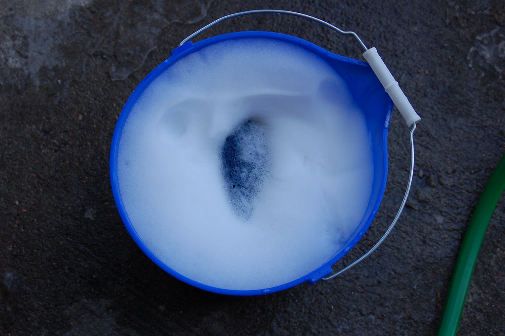 洗剤の泡で満たされた青いバケツとホース